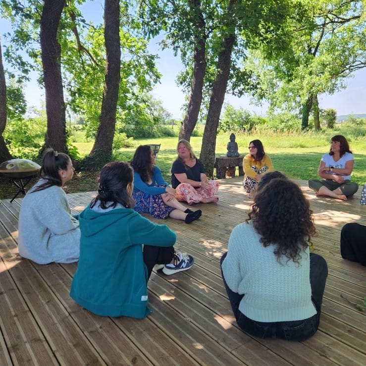Cercle Photos de plusieurs personnes assises en tailleur devant la yourte. Plusieurs arbres en fond