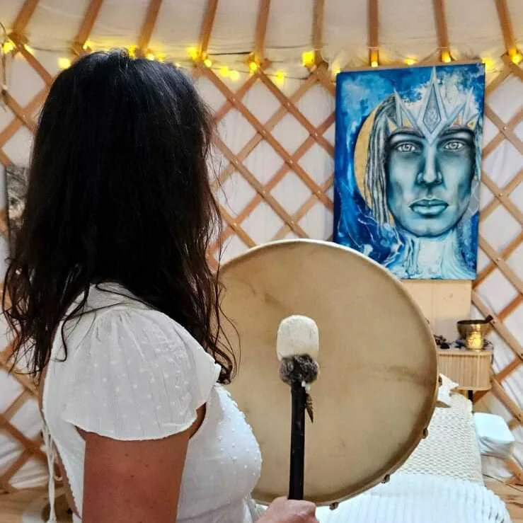 Soin Une femme se tient debout dans la yourte, face à un tableau. Elle tient dans sa main un tambour